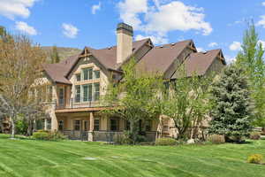 Back of property with stucco siding, a yard, a chimney, and roof with shingles