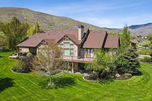 Back of house featuring a chimney, a lawn, a mountain view, and a patio