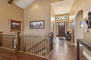 Entrance foyer with hardwood / wood-style floors, a chandelier, baseboards, high vaulted ceiling, and arched walkways