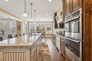 Kitchen featuring appliances with stainless steel finishes, a sink, dark wood-style flooring, a kitchen island with sink, and light stone countertops