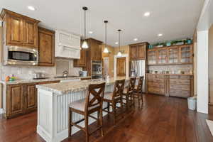 Kitchen featuring stainless steel appliances, brown cabinetry, tasteful backsplash, a kitchen island with sink, and dark wood-style floors