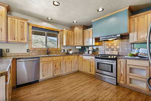Kitchen featuring light brown cabinetry, appliances with stainless steel finishes, a textured ceiling, tasteful backsplash, and light wood-type flooring