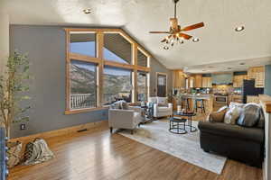 Living area featuring a textured ceiling, ceiling fan, light wood-style flooring, and high vaulted ceiling