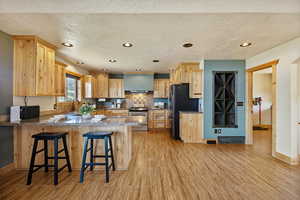 Kitchen with a peninsula, light brown cabinets, light wood-type flooring, stainless steel stove, and recessed lighting