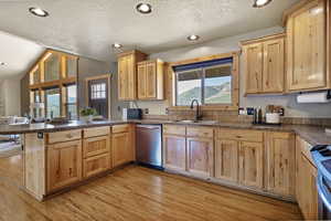 Kitchen with a peninsula, stainless steel dishwasher, a textured ceiling, light wood-style floors, and dark countertops