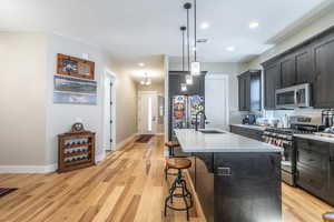 Kitchen featuring stainless steel appliances, a sink, a kitchen breakfast bar, light countertops, and light wood-style floors