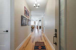 Hall with light wood-style floors, a chandelier, baseboards, and recessed lighting