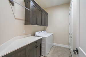 Washroom featuring cabinet space, washing machine and dryer, light tile patterned flooring, and baseboards