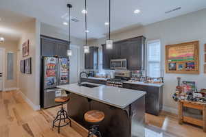 Kitchen with appliances with stainless steel finishes, a sink, light wood-style floors, light countertops, and a kitchen breakfast bar