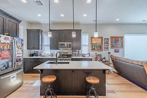 Kitchen with appliances with stainless steel finishes, a sink, light wood-type flooring, light countertops, and recessed lighting