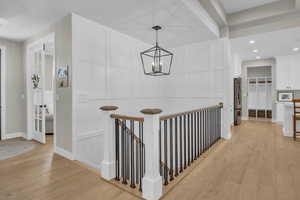 Corridor with light wood-style floors, a chandelier, baseboards, a decorative wall, and recessed lighting