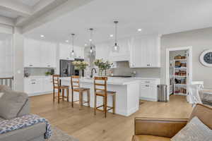 Kitchen featuring stainless steel fridge with ice dispenser, open floor plan, light wood-style floors, light countertops, and recessed lighting