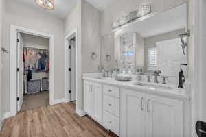 Full bathroom with wood finished floors, double vanity, a spacious closet, and baseboards