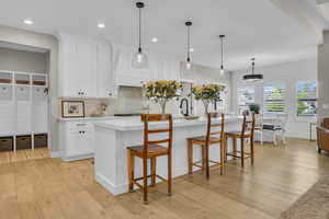 Kitchen with light countertops, tasteful backsplash, light wood-style flooring, white cabinetry, and an island with sink