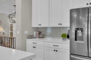 Kitchen featuring stainless steel fridge, backsplash, white cabinets, and a chandelier