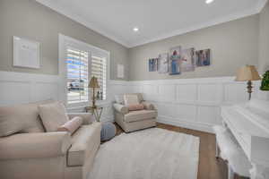 Living area featuring wood finished floors, a decorative wall, a wainscoted wall, recessed lighting, and crown molding