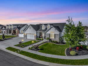 View of front of house featuring board and batten siding, stone siding, an attached garage, concrete driveway, and a front lawn