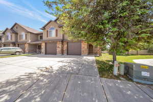 View of front facade with concrete driveway, an attached garage, stone siding, stucco siding, and a front lawn