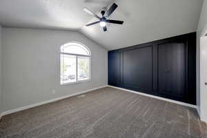 Carpeted empty room with ceiling fan, vaulted ceiling, baseboards, and a textured ceiling