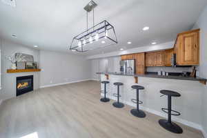 Kitchen with stainless steel appliances, a kitchen breakfast bar, light wood-style floors, brown cabinets, and recessed lighting