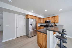 Kitchen with stainless steel appliances, a peninsula, light wood-style flooring, a breakfast bar area, and baseboards