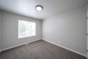 Spare room featuring dark carpet and baseboards