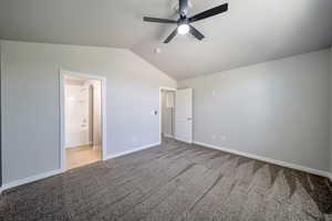 Unfurnished bedroom with carpet floors, vaulted ceiling, baseboards, ensuite bath, and a ceiling fan