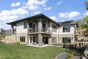 Back of property featuring a balcony, stone siding, a patio, a lawn, and a mountain view