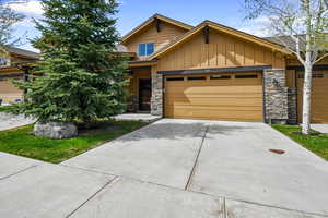 View of front of property featuring board and batten siding, stone siding, driveway, and an attached garage