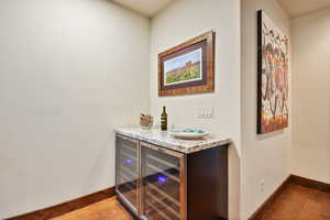Indoor dry bar with wood finished floors, baseboards, and beverage cooler