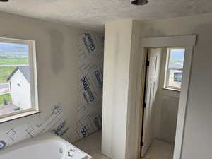 Bathroom featuring a textured ceiling and a tub to relax in