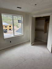 Unfurnished bedroom featuring multiple windows, baseboards, a textured ceiling, and a closet