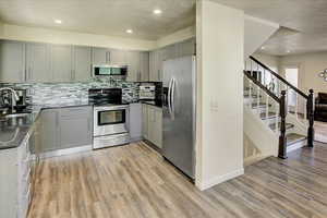 Kitchen with appliances with stainless steel finishes, gray cabinets, light wood-type flooring, a textured ceiling, and recessed lighting