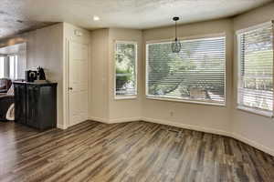 Unfurnished dining area with wood finished floors, plenty of natural light, baseboards, and a textured ceiling