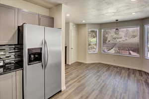 Kitchen featuring stainless steel fridge with ice dispenser, light wood-style floors, a textured ceiling, gray cabinetry, and backsplash