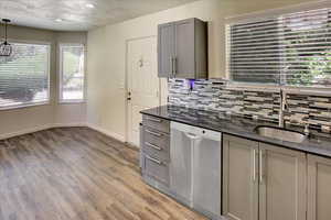 Kitchen featuring stainless steel dishwasher, gray cabinets, tasteful backsplash, a sink, and light wood finished floors