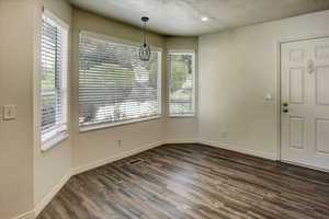Unfurnished dining area with plenty of natural light, dark wood-type flooring, a textured ceiling, baseboards, and recessed lighting