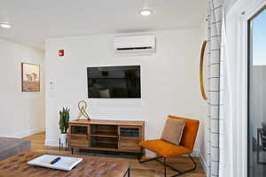 Living area with a wall mounted air conditioner, wood finished floors, baseboards, and recessed lighting