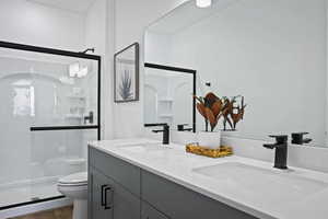 Bathroom with toilet, a stall shower, and double vanity