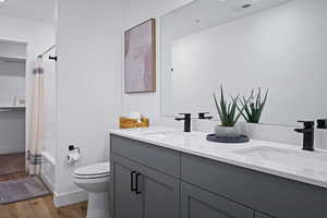 Bathroom featuring wood finished floors, toilet, double vanity, and baseboards