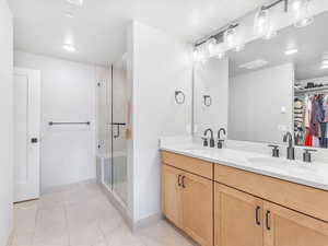 Full bathroom with tile patterned flooring, a spacious closet, baseboards, a shower stall, and double vanity