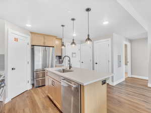 Kitchen with stainless steel appliances, light brown cabinets, a sink, light wood-style flooring, and light countertops