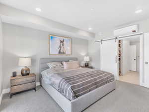 Carpeted bedroom with a wall mounted air conditioner, a barn door, recessed lighting, and baseboards