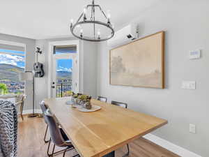 Dining room featuring a wall unit AC, a chandelier, light wood-style floors, and baseboards