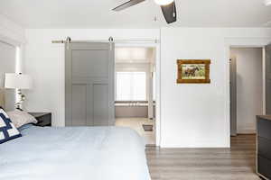 Bedroom featuring light wood finished floors, baseboards, ensuite bath, a ceiling fan, and a barn door