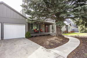 View of front of house with covered porch, a chimney, driveway, board and batten siding, and a garage