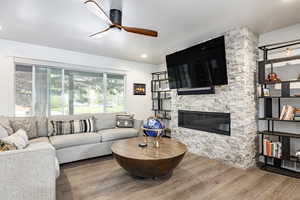 Living area with a ceiling fan, wood finished floors, and a fireplace