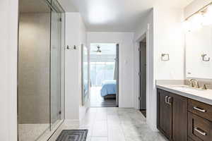 Ensuite bathroom with a stall shower, ceiling fan, vanity, tile patterned flooring, and baseboards