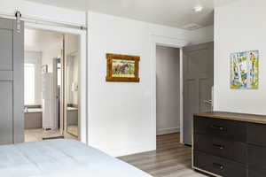 Bedroom with light wood-type flooring, ensuite bathroom, and baseboards
