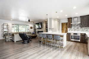 Kitchen featuring stainless steel oven, wall chimney range hood, open floor plan, dark brown cabinetry, and light wood-style floors